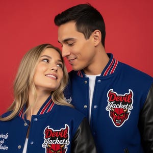 May include: A couple wearing blue and black letterman jackets with the words "Devil Jackets" and a devil mascot patch. The jackets have red and white striped trim on the collar and cuffs. The background is a solid red.