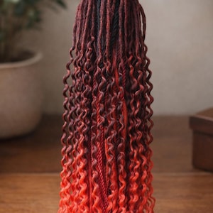 May include: A bundle of ombre-colored synthetic dreadlocks. The dreadlocks transition from dark brown to red and then to bright orange at the ends. The hair is styled with tight, defined curls.