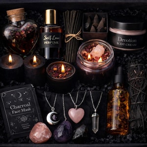 Könnte beinhalten: Eine schwarze Box mit Selbstpflegeartikeln. Enthält eine herzförmige Flasche, Parfüm, Kerzen, Räucherstäbchen, eine Gesichtsmaske, Körpercreme, Halsketten mit Anhängern und ätherisches Öl. Die Box ist mit schwarzem Papier gefüllt.
