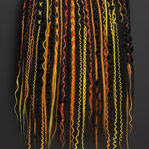 May include: A collection of black, orange, and yellow dreadlocks. The dreadlocks vary in texture, including straight, wavy, and braided styles. Some are adorned with decorative stitching. The color palette is vibrant, with a mix of warm tones.