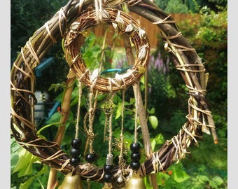 Puede incluir: Un adorno de pared artesanal en forma de espiral, hecho de ramitas y cuerda tejidas. Presenta una corona circular más pequeña, llaves colgantes, cuentas negras y tres campanas de latón. Los tonos naturales crean una estética rústica y bohemia.