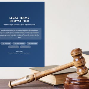 May include: A wooden gavel rests on a wooden block, beside a stack of books. A blue poster titled "Legal Terms Demystified" is in the background. The poster is a quick reference guide for legal assistants.