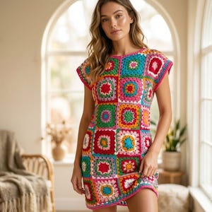 May include: A colorful, handmade crochet dress featuring a patchwork design. The dress is composed of various squares in vibrant colors like pink, blue, green, and orange, with a pink trim around the neckline and sleeves. The dress is knee-length.