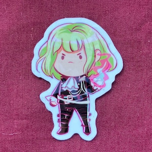 Peut inclure: Un autocollant représentant un personnage de dessin animé aux cheveux verts et à l'expression sévère. Le personnage porte une tenue noire avec des détails blancs et un contour bleu clair. Le personnage tient un effet d'énergie rose et bleu.