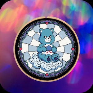 Może przedstawiać: Haft krzyżykowy przedstawiający niebieskiego Care Bear siedzącego na chmurze, oprawiony w drewnianą tamborkę. Miś ma zrzędliwą minę i wzór w kształcie serca na brzuchu. Tło jest w stylu witrażu z wzorem w szachownicę.