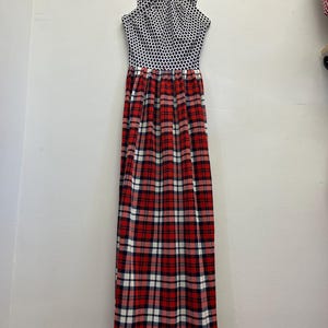 May include: A striking maxi dress with a distinctive design. The bodice has a black and white polka dot pattern, and the skirt displays a red, white, and navy plaid design. The dress is suspended from a wooden hanger.