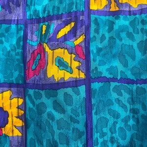 May include: Close-up of a fabric with a vibrant, abstract pattern. The design features a grid of squares in teal, purple, and yellow. Some squares have a leopard print, while others have floral shapes in pink and yellow.