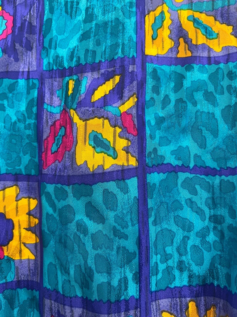 May include: Close-up of a fabric with a vibrant, abstract pattern. The design features a grid of squares in teal, purple, and yellow. Some squares have a leopard print, while others have floral shapes in pink and yellow.