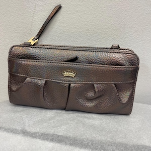 May include: A metallic brown clutch bag with a textured finish. The bag features a front pocket with pleated detailing and a gold-coloured crown emblem. It has a wrist strap and a zip closure.
