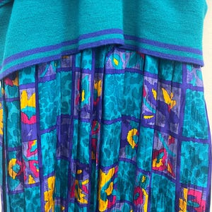 May include: A teal and purple vintage dress with a unique design. The top is a solid teal knit, while the skirt features a patterned design with teal, purple, yellow, and pink accents. The dress has a layered look.