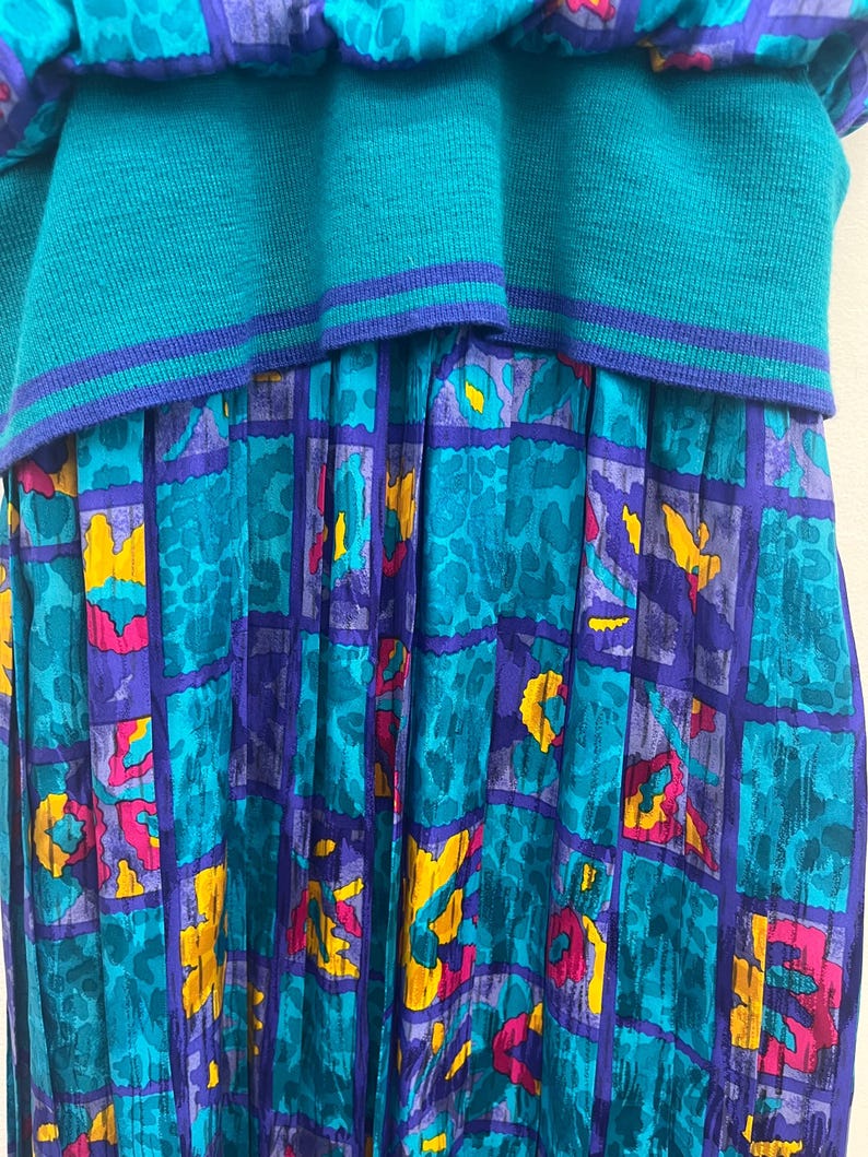 May include: A teal and purple vintage dress with a unique design. The top is a solid teal knit, while the skirt features a patterned design with teal, purple, yellow, and pink accents. The dress has a layered look.