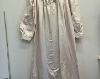 Könnte beinhalten: Langes, hellrosa Satin-Nachthemd mit zartem weißem Spitzenkragen und Manschetten. Das Nachthemd hat lange Ärmel und eine Knopfleiste vorne. Es hängt an einem Holzkleiderbügel.