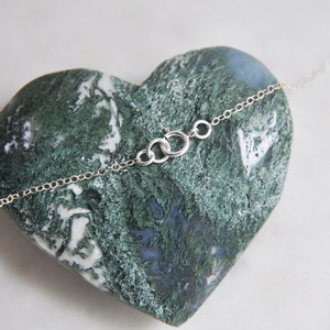 Puede incluir: Un delicado collar de plata con una peque&ntilde;a cadena y cierre, apoyado sobre una piedra verde y azul en forma de coraz&oacute;n. El collar es sencillo y elegante, ideal para el uso diario.