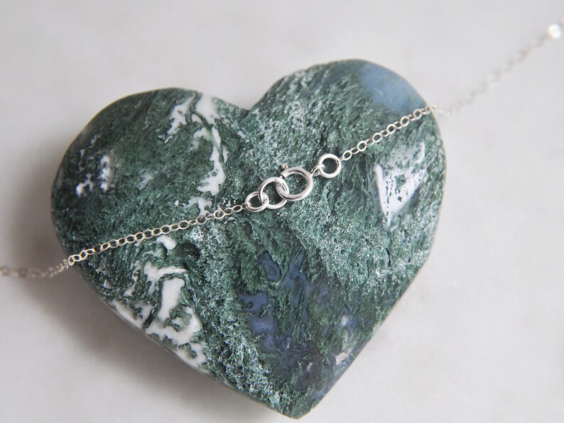 Puede incluir: Un delicado collar de plata con una peque&ntilde;a cadena y cierre, apoyado sobre una piedra verde y azul en forma de coraz&oacute;n. El collar es sencillo y elegante, ideal para el uso diario.