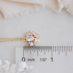 May include: A gold-colored necklace with a pendant featuring an oval-shaped clear stone surrounded by smaller, pear-shaped clear stones. The pendant is approximately 0.75 inches in diameter. The necklace is displayed on a white surface.