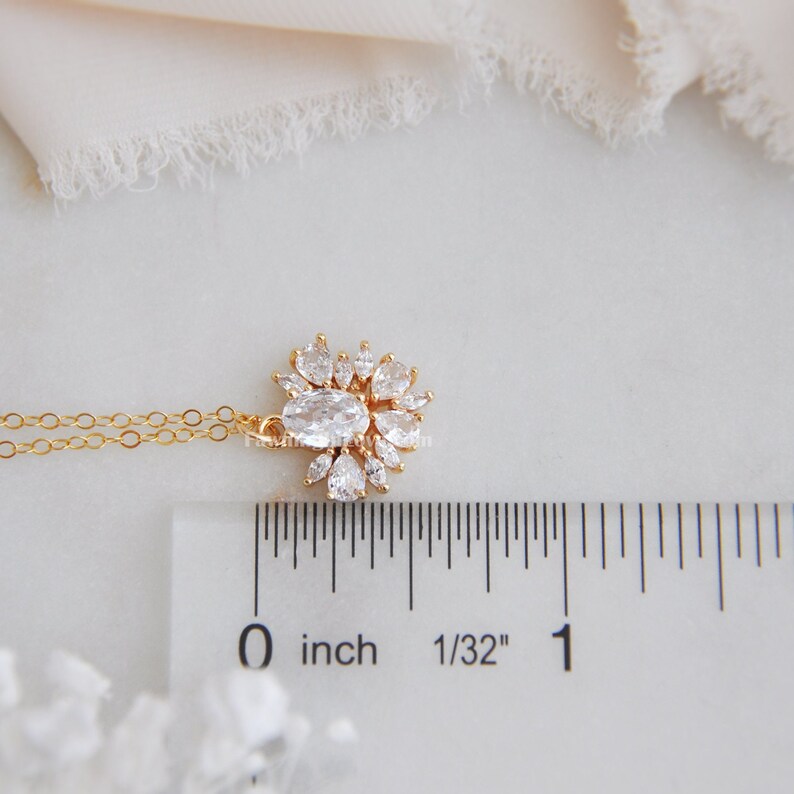 May include: A gold-colored necklace with a pendant featuring an oval-shaped clear stone surrounded by smaller, pear-shaped clear stones. The pendant is approximately 0.75 inches in diameter. The necklace is displayed on a white surface.