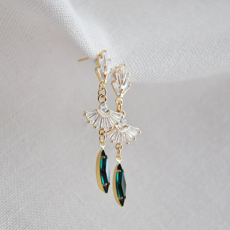 May include: Gold-toned drop earrings featuring a fan-shaped design with clear crystals and emerald green teardrop-shaped gems. The earrings have a post-back closure and are displayed against a white background.