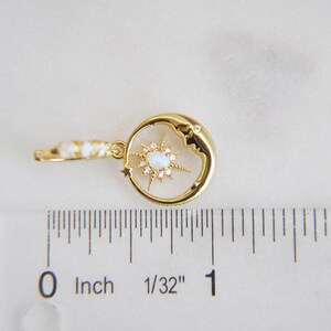 Op de afbeelding: Goudkleurige oorbel met een hemels thema, met een halve maan met een sterrenpatroon. De ster heeft een centrale opaalachtige steen en is omgeven door kleine, heldere kristallen. De oorbel is ongeveer 2,5 cm lang.