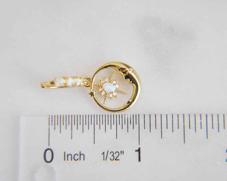 Op de afbeelding: Goudkleurige oorbel met een hemels thema, met een halve maan met een sterrenpatroon. De ster heeft een centrale opaalachtige steen en is omgeven door kleine, heldere kristallen. De oorbel is ongeveer 2,5 cm lang.