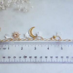 May include: Gold-toned celestial charm bracelet featuring a crescent moon, stars, and sunburst pendant. The bracelet is approximately 6 inches long and includes a chain extender. The charms are attached to a delicate chain.