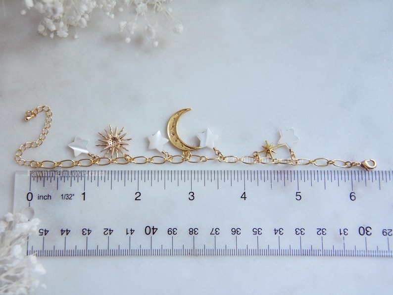May include: Gold-toned celestial charm bracelet featuring a crescent moon, stars, and sunburst pendant. The bracelet is approximately 6 inches long and includes a chain extender. The charms are attached to a delicate chain.