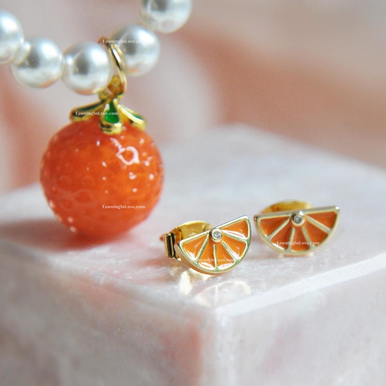 Crystal pearl necklace featuring a detailed orange fruit pendant. The fruit necklace comes with gold orange slice stud earrings accented with single cz charm in the center.