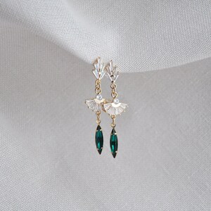 May include: Gold-toned drop earrings with a fan-shaped design, adorned with clear crystals and emerald green teardrop-shaped gems. The earrings have a delicate, elegant appearance, suitable for special occasions.