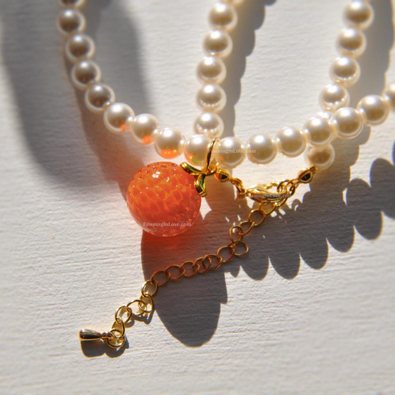 Crystal pearl necklace featuring a detailed orange fruit pendant. The fruit necklace comes with gold orange slice stud earrings accented with single cz charm in the center.
