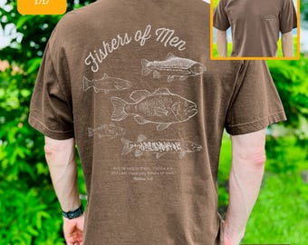 May include: Espresso-colored t-shirt with a graphic of several fish and the words "Fishers of Men" in white script. The shirt also features a Bible verse. The Comfort Colors 1717 shirt is a short-sleeved tee.