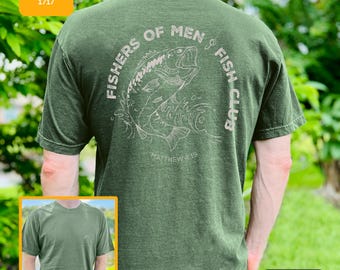 May include: Green t-shirt with a graphic of a fish and the words "Fishers of Men Fish Club" printed on the back. The text "Matthew 4:19" is below the fish graphic. The shirt is a solid green color.