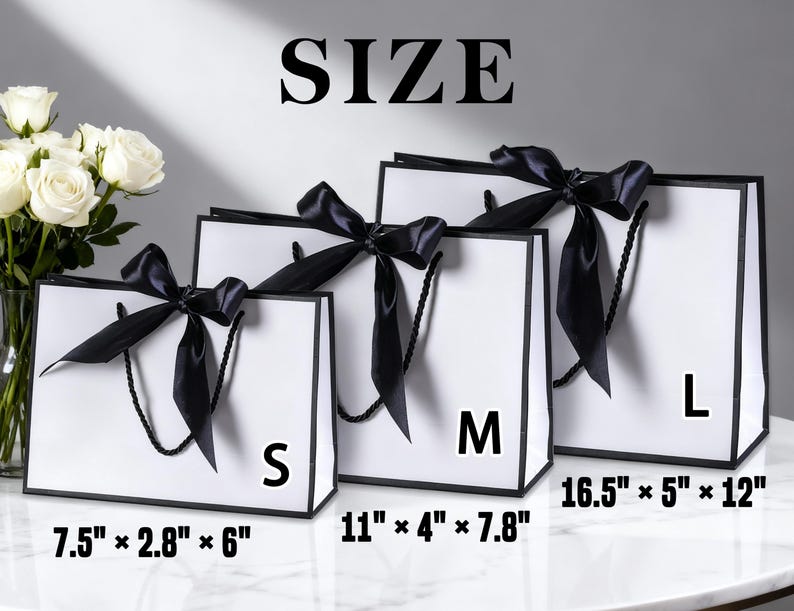 Pu&ograve; includere: Tre sacchetti regalo bianchi con bordi e manici neri, ognuno ornato da un fiocco di raso nero. Le taglie sono S, M e L, con dimensioni di 19cm x 7cm x 15cm, 28cm x 10cm x 20cm e 42cm x 13cm x 30cm. La parola "SIZE" &egrave; in alto.