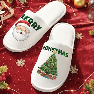 Peut inclure: Paire de pantoufles de Noël blanches. L'une présente le Père Noël avec le mot "MERRY" en vert. L'autre affiche un sapin de Noël décoré avec le mot "CHRISTMAS" en vert.