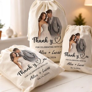 Puede incluir: Tres bolsas de cordón de color crema con una imagen impresa de una pareja de novios. Las bolsas tienen el texto "Thank you" y "For celebrating with us!" junto con nombres y una fecha. Las bolsas están atadas con un cordón de color natural.