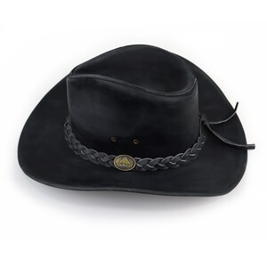 May include: A black leather hat with a wide brim and a braided band around the crown. The hat features a small, circular metal emblem and is designed in a classic style. The hat is a dark color and appears to be made of a durable material.