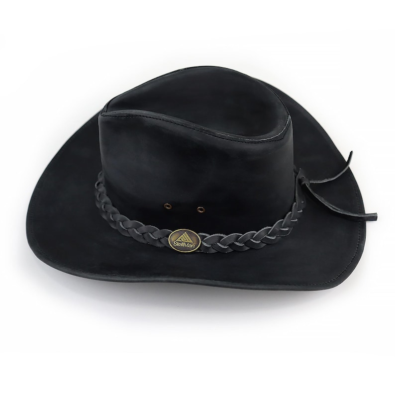 May include: A black leather hat with a wide brim and a braided band around the crown. The hat features a small, circular metal emblem and is designed in a classic style. The hat is a dark color and appears to be made of a durable material.