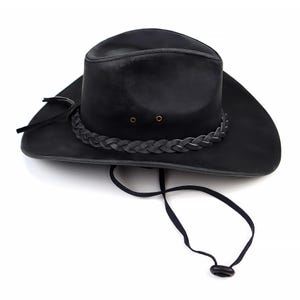 May include: Black leather cowboy hat with a braided band around the crown and a chin strap. The hat has a wide brim and a classic western design. The hat is made of a durable material and is suitable for outdoor wear.