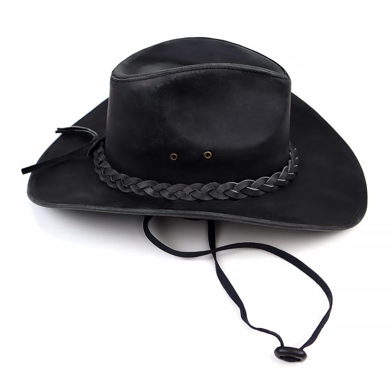 May include: Black leather cowboy hat with a braided band around the crown and a chin strap. The hat has a wide brim and a classic western design. The hat is made of a durable material and is suitable for outdoor wear.