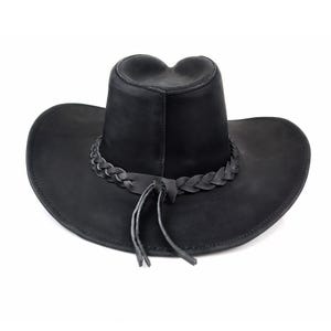 May include: Black cowboy hat with a braided leather band around the crown and a chin strap. The hat has a wide brim and a teardrop-shaped crown. The hat is made of a matte black material.