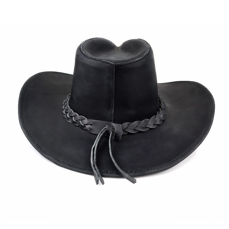 May include: Black cowboy hat with a braided leather band around the crown and a chin strap. The hat has a wide brim and a teardrop-shaped crown. The hat is made of a matte black material.