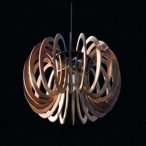 May include: A modern, wooden pendant light fixture with a unique, layered design. The light features multiple concentric, circular wooden rings, creating an open, airy structure. The fixture hangs from a single wire against a dark background.