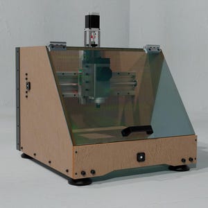 May include: A desktop CNC milling machine featuring a light brown wooden enclosure with a slanted transparent front panel. The device includes a top-mounted motor, internal metal rails, a black handle on the front, and four black circular feet.