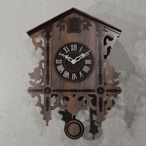 Könnte beinhalten: Dunkelbraune Kuckucksuhr aus Holz. Das Zifferblatt hat römische Ziffern und weiße Zeiger. Die Uhr hat dekorative Schnitzereien und ein Pendel. Ein klassisches Wohnaccessoire, etwa 30 cm hoch.