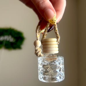 May include: A clear, diamond-patterned glass bottle with a wooden cap and a decorative rope and ribbon. The ribbon is yellow with black polka dots. The bottle is designed to hold fragrance.