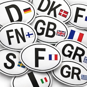 Op de afbeelding: Een verzameling witte ovale stickers met zwarte letters en landenvlaggen. De stickers tonen landcodes zoals GB, D, F en GR, met bijbehorende vlaggen van het Verenigd Koninkrijk, Duitsland, Frankrijk en Griekenland.
