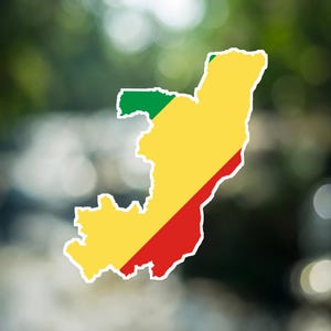 Op de afbeelding: Een sticker in de vorm van de kaart van de Republiek Congo, met de nationale vlagkleuren groen, geel en rood in een diagonaal patroon met een dikke witte rand tegen een wazige, onscherpe achtergrond.