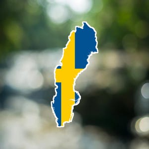 Può includere: Un adesivo a forma di mappa della Svezia con il design della bandiera nazionale, caratterizzato da uno sfondo blu e una croce gialla. L'adesivo presenta un bordo bianco distinto che delinea l'intera forma del paese su uno sfondo sfocato.