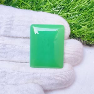 May include: A rectangular, polished green gemstone with a smooth, flat surface and rounded corners. The stone displays a vibrant, solid emerald-green hue with a high-gloss finish that reflects light across its top surface, showcasing a uniform colour.