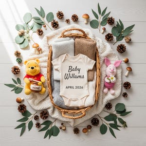 May include: A baby announcement featuring a cream-colored onesie with the text "Baby Willams APRIL 2026" inside a wicker basket with folded blankets. The arrangement includes Winnie the Pooh, Piglet, pinecones, eucalyptus, and mushrooms.