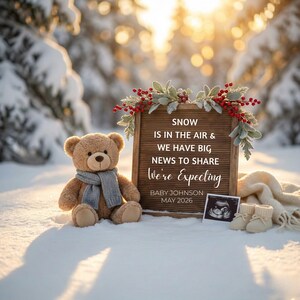May include: A teddy bear wearing a gray scarf sits in the snow next to a wooden sign with the text "SNOW IS IN THE AIR & WE HAVE BIG NEWS TO SHARE We're Expecting BABY JOHNSON MAY 2026". A sonogram and baby booties are also in the snow.