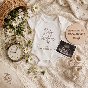 Pode incluir: Um body de bebé branco canelado com o texto Baby Williams, um ícone de coração e DUE SEPTEMBER 2027. Inclui um disco de madeira com PLOT TWIST: We're Having Baby!, uma ecografia, sapatinhos de malha creme, um relógio e margaridas.